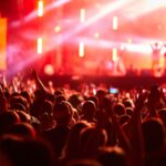 Audience with raised hands watching a live concert under colorful stage lighting.