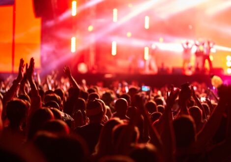 Audience with raised hands watching a live concert under colorful stage lighting.